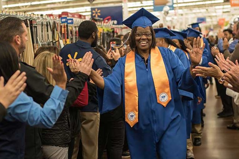 A Walmart associate receives high-fives as she enters an academy graduation.
