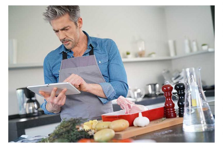 A man prepares meat using an online recipe.