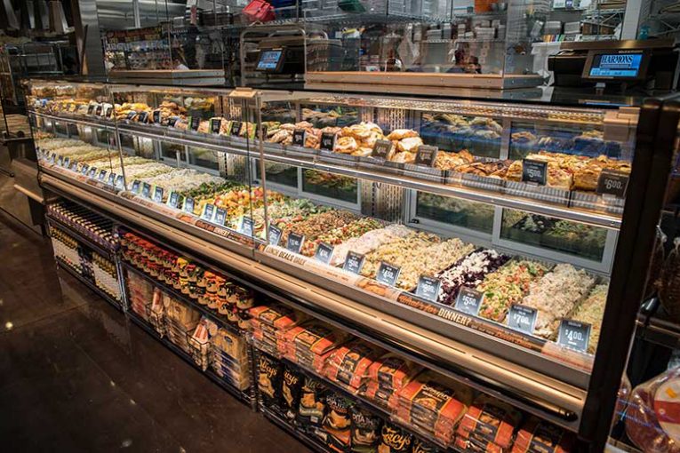 The Harmons Holladay Market in Holladay, Utah, features a Lunch Deals Daily and “What’s for Dinner?” case that holds a range of by-the-pound prepared foods and bakery items as well as center store items down below.