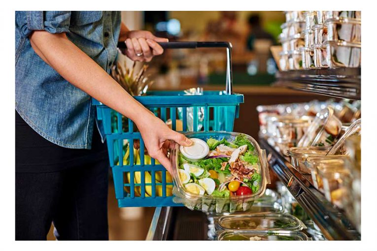 A woman picking up a prepared salad from a cold case