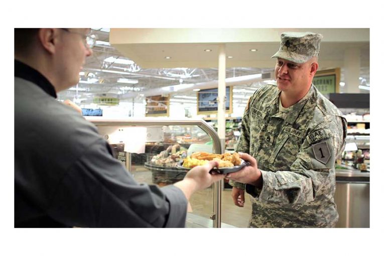 A Reasor's employee hands a plate of food to a man in a military uniform.